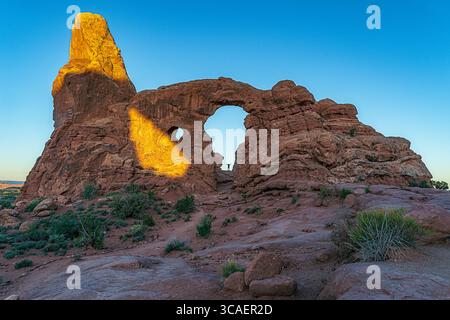 Ein Besucher wird vom Turret Arch im Arches National Park in den Schatten gestellt. Der Park ist bekannt für seine beeindruckenden Sandsteinformationen. Stockfoto