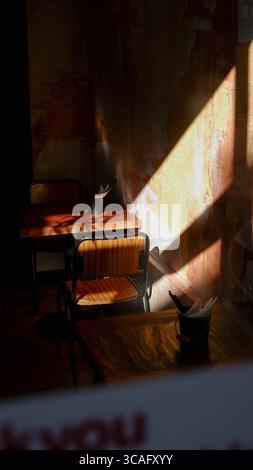 Warmes Sonnenlicht zieht durch ein Fenster und wirft lange Schatten über rustikale Holztische und -Stühle in einer ruhigen Caféecke Stockfoto
