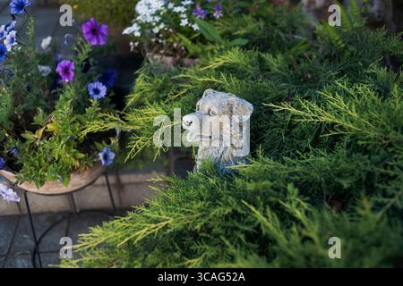 Hundestatue umgeben von Blumen und grünen Sträuchern Stockfoto