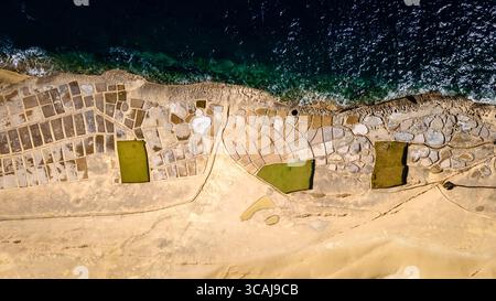 Blick von oben auf traditionelle Salinen, die in die Kalksteinküste von Gozo, Malta, mit türkisfarbenem mediterranem Wasser gehauen wurden. Stockfoto