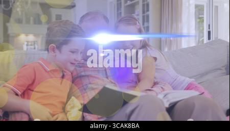 Großvater liest ein offenes Buch mit Enkelkindern auf Sofa im Wohnzimmer, mit Kamin Stockfoto