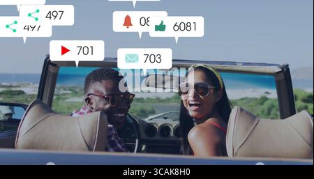 Sitzendes Paar mit Sonnenbrille, schwebende soziale Ikonen im Cabriolet auf der Küstenstraße Stockfoto