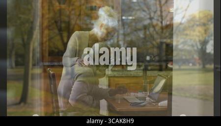 Seniorenpaar, das an einem Laptop in der Küchenecke arbeitet, mit Hoodie und Strickjacke Stockfoto