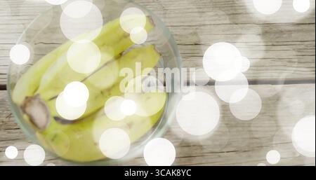 Glasschale mit gelben Bananen auf Holztisch, mit rundem, helles Bokeh, Kopierraum Stockfoto