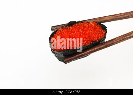 Nahaufnahme eines einzelnen, perfekt gefertigten Sushi-Gunkan-Makis mit Reis, Nori und Tobiko (fliegender Fischrogen), die zart von Essstäbchen gehalten werden. Stockfoto