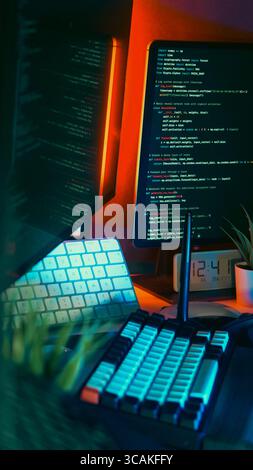 Erweiterte Kodierpult-Einrichtung mit mehreren Monitoren mit farbenfroher beleuchteter Tastatur und sichtbarem Quellcode auf mehreren Bildschirmen. Futuristische Softwareentwickler Stockfoto