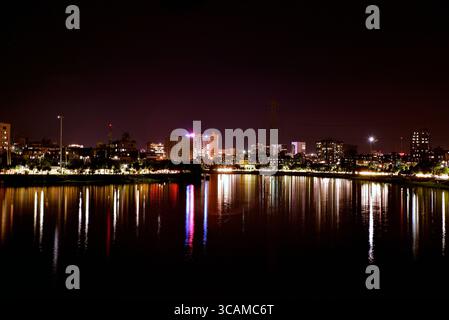 Ein atemberaubender Blick bei Nacht auf den Hatirjheel See in Dhaka, Bangladesch, mit einer modernen beleuchteten Skyline und farbenfrohen Lichtern, die sich auf dem Wasser spiegeln. Stockfoto