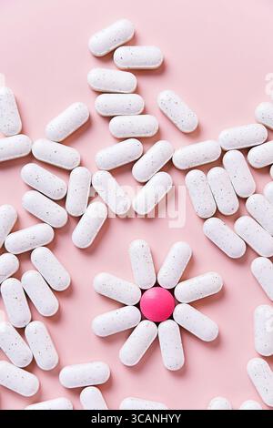 Kreative Anordnung von weißen Pillen und einer rosa, die eine Blume auf rosa Hintergrund bilden. Gesundheitsbegriff, Nahrungsergänzungsmittel und kreative Medizin Stockfoto