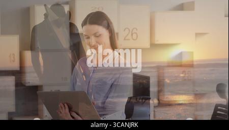 Geschäftsfrau in Bluse mit Laptop im Büro mit Sonnenuntergang Ozeanpaneelen und Mann im Fedora-Mantel Stockfoto