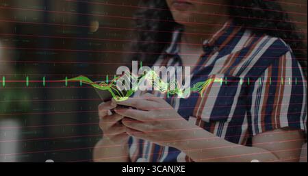 Das Smartphone in der Hand, eine Frau mit gestreiftem Hemd, die auf dem Balkon die Finanzkarte analysiert Stockfoto