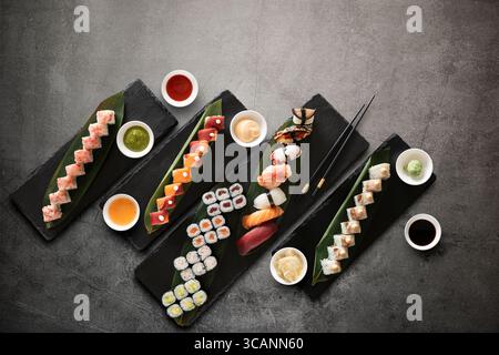 Sushi-Brötchen mit Reis, Fisch und Saucen auf dunklem Steinhintergrund. Draufsicht mit Kopierbereich. Stockfoto