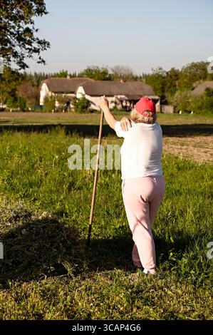 Landwirtin, die sich auf einen Rechen stützt, während sie Heu auf einem Feld erntet, Rückansicht Stockfoto