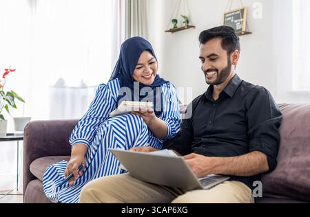 Muslimisches Paar, das zu Hause einen Laptop auf dem Sofa benutzt Stockfoto