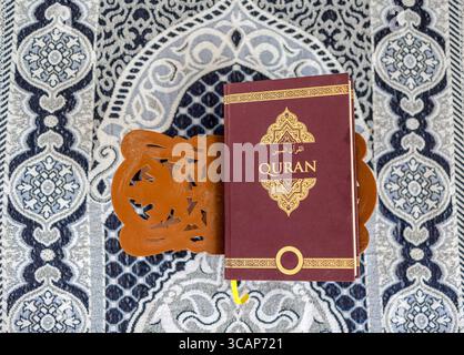 Heiliger Koran auf hölzernem Rehal auf islamischer Gebetsmatte, Blick von oben Stockfoto