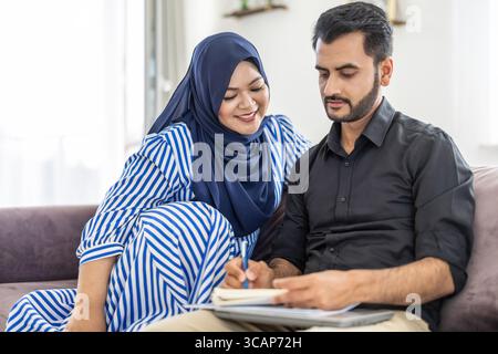 Glückliches muslimisches Paar, das zu Hause auf dem Sofa sitzt Stockfoto