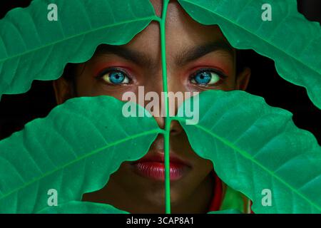 Mirsharai, Bangladesch - 20. September 2020: Blick auf die markanten blauen Augen einer jungen Frau, die durch ein leuchtendes grünes Laub stechen, ein fesselnder Kontrast Stockfoto