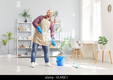Porträt eines lächelnden Mannes, der fröhlich auf die Kamera blickt, den Mopp in der Hand hält und das Haus oder das Büro wischt. Stockfoto