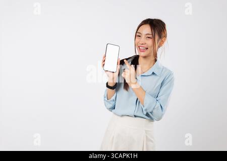 Eine glückliche asiatische Frau zeigt ihr Handy und zeigt mit dem Finger auf das Display Stockfoto