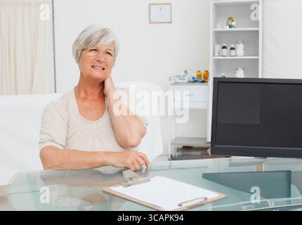 Ältere Patientin sitzt am Glasschreibtisch im Klinikzimmer, liest Klemmpapier, Kopierraum Stockfoto