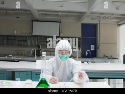 Overall-Schutzanzug auf Labortisch mit konischem Kolben aus grüner Lösung und Bechergläsern Stockfoto