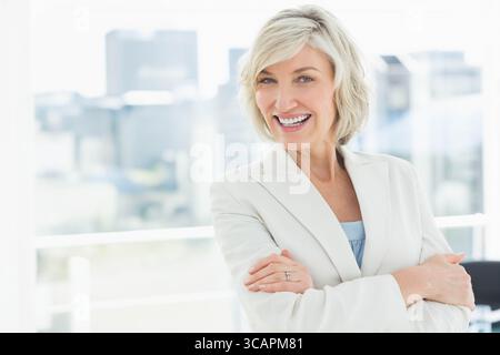 Frau mittleren Alters, die mit überkreuzten Armen im Büro steht, am Fenster mit Blick auf die Skyline, Kopierraum Stockfoto