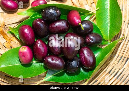 Jamun- oder Syzygium Cumini-Frucht mit Blättern in einem Bambuskorb auf hölzernem Hintergrund Stockfoto