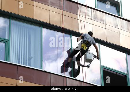 Hochhausfensterreiniger zeigt Engagement bei der Arbeit an der Glasfassade in einer belebten städtischen Umgebung Stockfoto