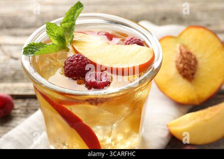 Erfrischender Eistee mit Pfirsich, Himbeeren und Minze im Glas auf dem Tisch, Nahaufnahme Stockfoto