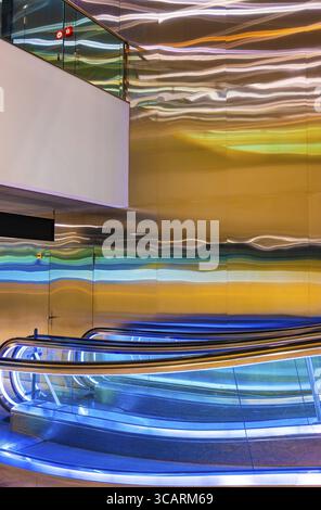 Innen beleuchteter Flughafen Zürich mit Eskalator und einer Wand mit Lichtreflexion bei Nacht im Flughafen Kloten, Zürich, Kanton Zürich, Schweiz Stockfoto