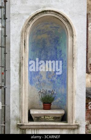 Ein Blumenstrauß verwelkt Lavendel Blumen für die heilige Jungfrau Maria im blinden Fenster der alten Backsteinkirche Stockfoto