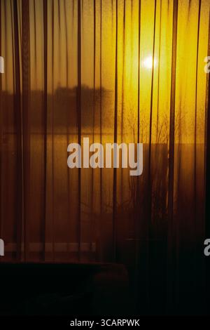 Warmes, goldenes Sonnenlicht durchströmt durchscheinende Vorhänge und ein nebeliges Fenster und schafft eine friedliche Abendatmosphäre mit weichen Schatten und gemütlicher Atmosphäre Stockfoto