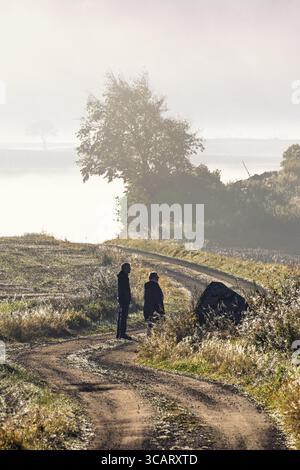 Zwei Personen laufen an einem nebeligen Herbsttag auf einer kurvenreichen Schotterstraße auf dem Land Stockfoto