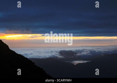 Ein atemberaubender Blick auf den Sonnenaufgang von einem Berggipfel aus, mit Wolken, die das Tal darunter bedecken, und goldenem Licht, das sich über den Himmel ausbreitet Stockfoto