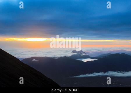 Ein atemberaubender Blick auf den Sonnenaufgang von einem Berggipfel aus, mit Wolken, die das Tal darunter bedecken, und goldenem Licht, das sich über den Himmel ausbreitet Stockfoto