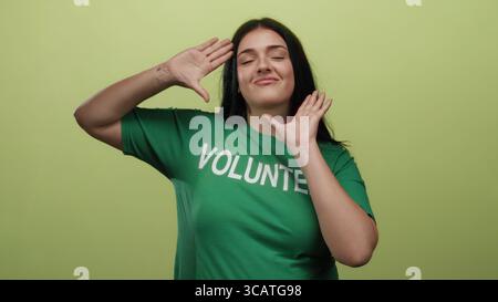 Junge Frau im grünen Freiwilligenhemd posiert spielerisch vor einem isolierten gelben Hintergrund und strahlt Vertrauen und Positivität in einem kurvigen Körperbild aus. Stockfoto