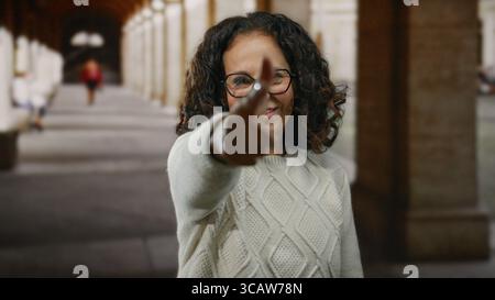 Frau mit lockigen Haaren, die tagsüber mit dem Finger auf spielerische Weise außerhalb des Gehweges des Universitätsgeländes gestickt hat Stockfoto