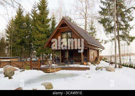 Grillplatz in der Nähe des hölzernen ländlichen Dorfhauses im gefrorenen Kiefernwald. Sonniger Sonnenaufgang im Dezember Stockfoto