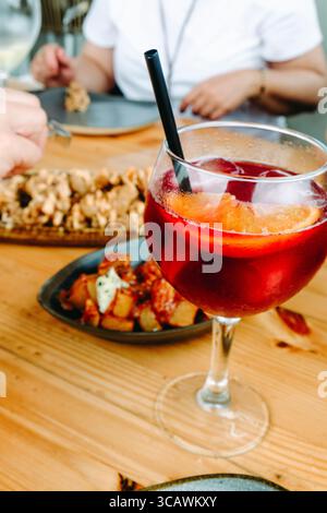 Nahaufnahme eines Glases Sangria mit Orangenscheiben, Patatas bravas und Chipirones a la andaluza auf dem Tisch, während die Menschen eine entspannte Mahlzeit genießen Stockfoto