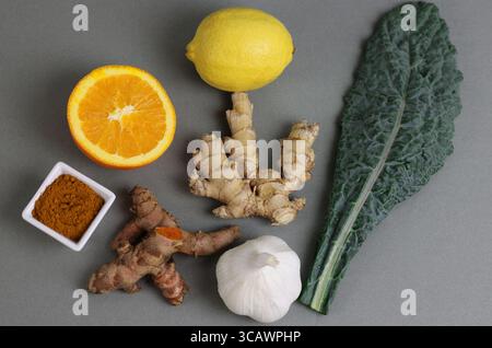 Entzündungshemmende Superfoods einschließlich Kurkuma, Knoblauch, Grünkohl, Ingwer, Zitrone, und orange auf grauem Hintergrund. Gesundes Lebensstil und Ernährungskonzept Stockfoto