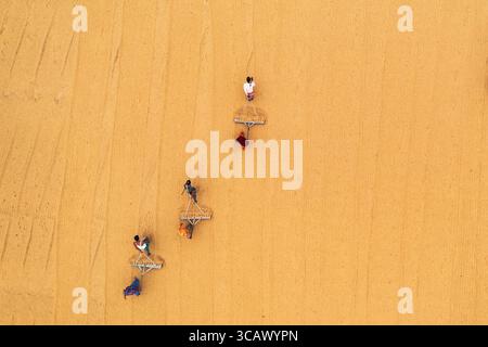 Bogura, Bangladesch - 24. Dezember 2018: Aus der Vogelperspektive verstreute Figuren über die Sandfläche, deren leuchtende Kleidung sich von der warmen, strukturierten Erde abhebt. Stockfoto