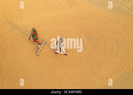 Bogura, Bangladesch - 24. Dezember 2018: Aus der Vogelperspektive sehen zwei Figuren, die goldene Körner harken und faszinierende konzentrische Muster auf dem weiten, sonnendurchfluteten Feld erzeugen. Stockfoto