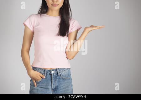 Eine junge Frau, ungefähr in den 20ern oder 30ern, steht vor einem schlichten, hellgrauen Hintergrund und blickt direkt an Stockfoto