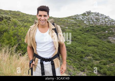 Ein Mann in seinen Zwanzigern, der auf einem schmalen Bergweg steht, einen Wanderstock hält und einen Rucksack trägt Stockfoto