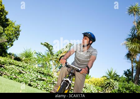 Mann in seinen 30ern, der mit gelbem Fahrrad über gepflegten Rasen fährt, mit blauem Helm, Kopierraum Stockfoto