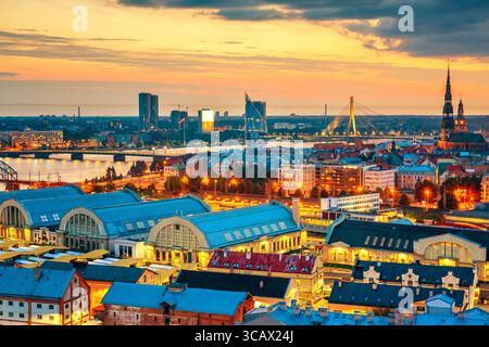 Wunderschönes Panorama von Riga Zentrum und Vansu Brücke über den Daugava Fluss während des atemberaubenden Sonnenuntergangs. Blick auf die beleuchtete Stadt Riga, die Hauptstadt von Lettland Stockfoto