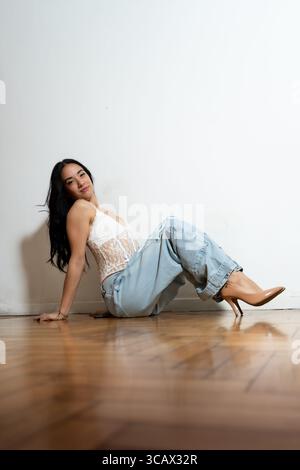 Das Model posiert auf einem Hartholzboden, trägt Jeans und ein Spitzenoberteil und zeigt zeitgenössischen urbanen Stil Stockfoto