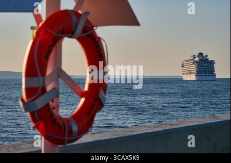 Kreuzfahrtschiff sichtbar am Horizont hinter rotem Rettungsschirm entlang der Küste von Danzig. Stockfoto