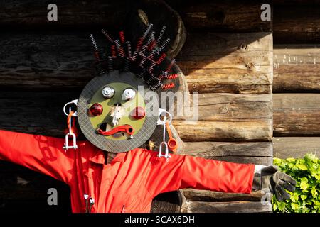 vogelscheuche aus Ersatzteilen mit rotem Overall gegen ein hölzernes Bauernhaus Stockfoto