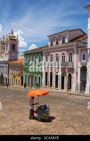 Farbenfrohe Colonial Street mit Verkäufer unter orangefarbenem Regenschirm auf dem Kopfsteinpflasterplatz in Salvador, Brasilien Stockfoto