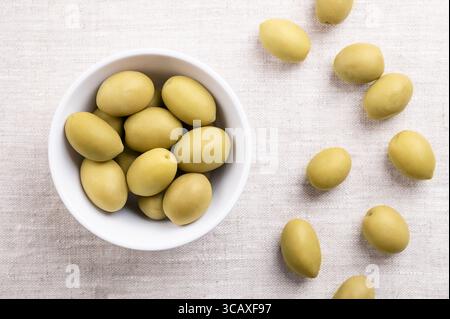 Grüne Oliven mit Grube, in einer weißen Schüssel auf Leinen. Ganze, große Tafeloliven, geerntet, bevor sie vollständig reif sind, mit einem würzigeren und salzigen Geschmack. Stockfoto